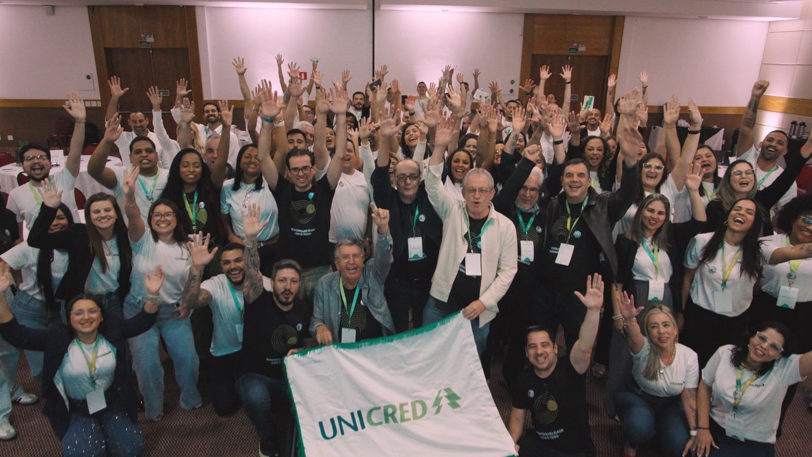 Colaboradores da Unicred Coalizão de braços erguidos, segurando a bandeira da cooperativa no Supera RJ